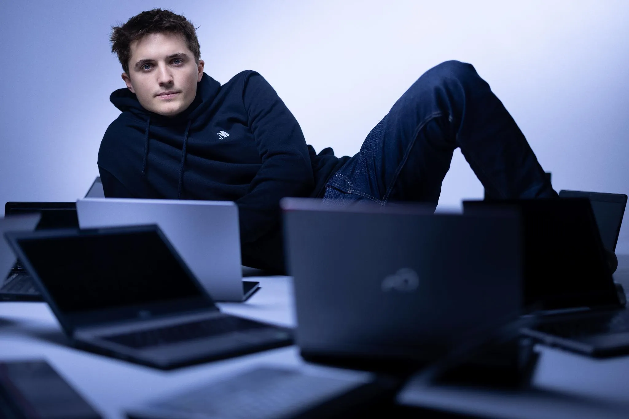 photo d'un homme aux cheveux bruns allongés sur le coté avec des ordinateurs devant lui