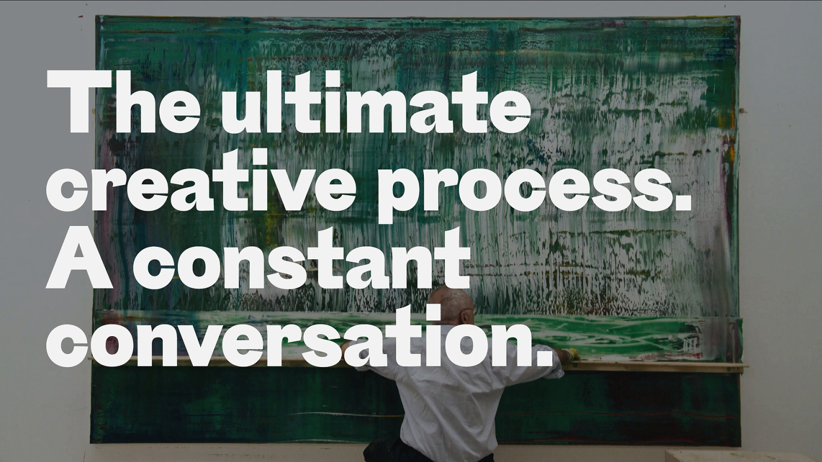 C'est une photo d'une slide de la présentation. On y voit Gerhard Richter assis face à une toile verte et bleue. Par dessus cette photo on y lit 'The ultimate creative process. A constant conversation' 